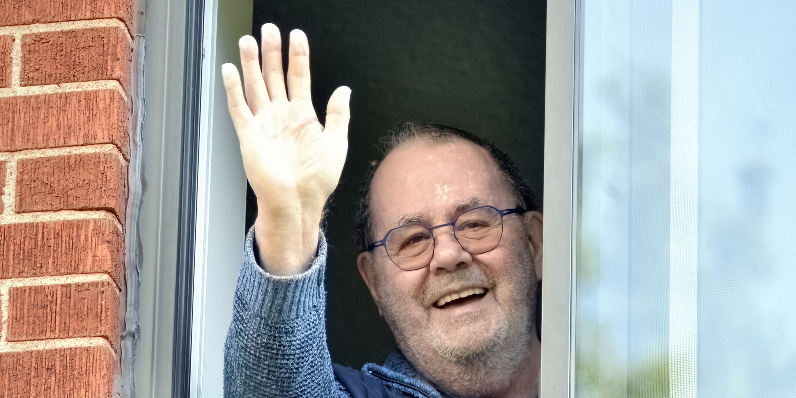 Un résident souriant saluant de la main à sa fenêtre
